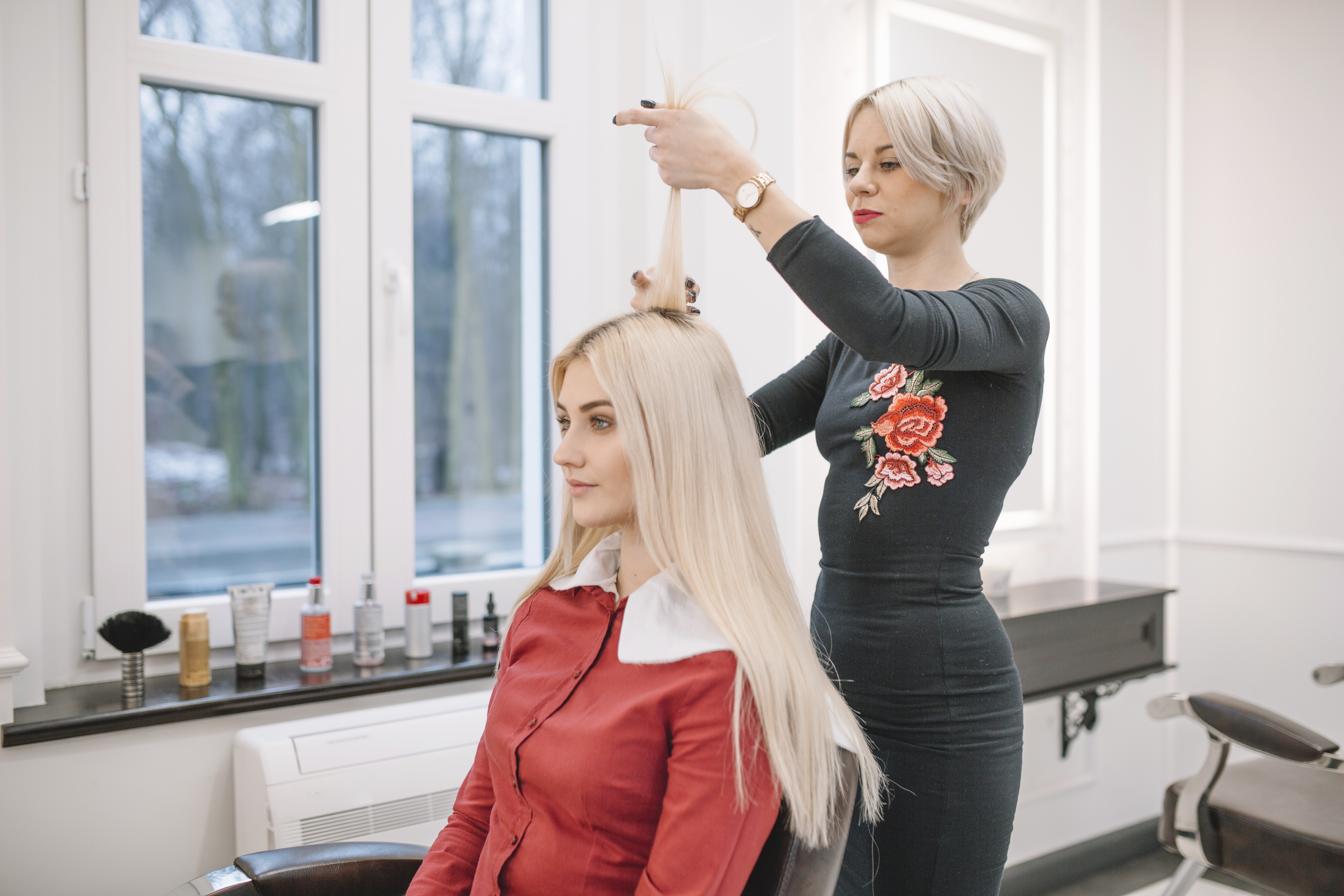 Cabeleireira em um salão iluminado analisando mechas de uma cliente loira, verificando a saúde dos fios após processos químicos e o uso de amônia no cabelo.